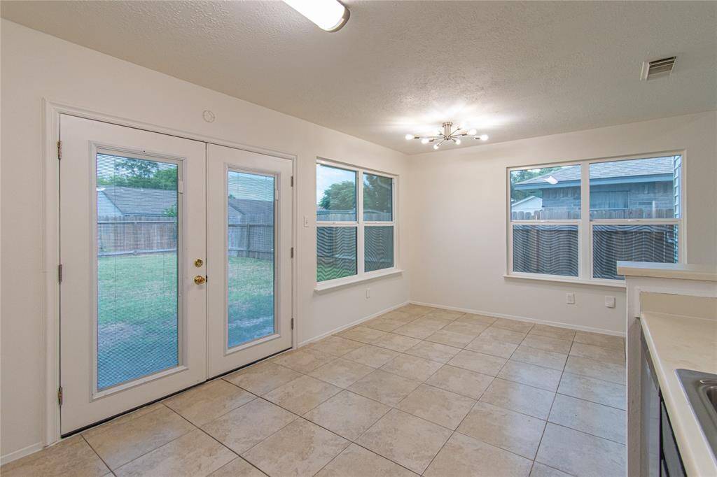 Bright dining area with large windows, French doors leading to a backyard, and tiled flooring. Modern light fixture adds elegance.
