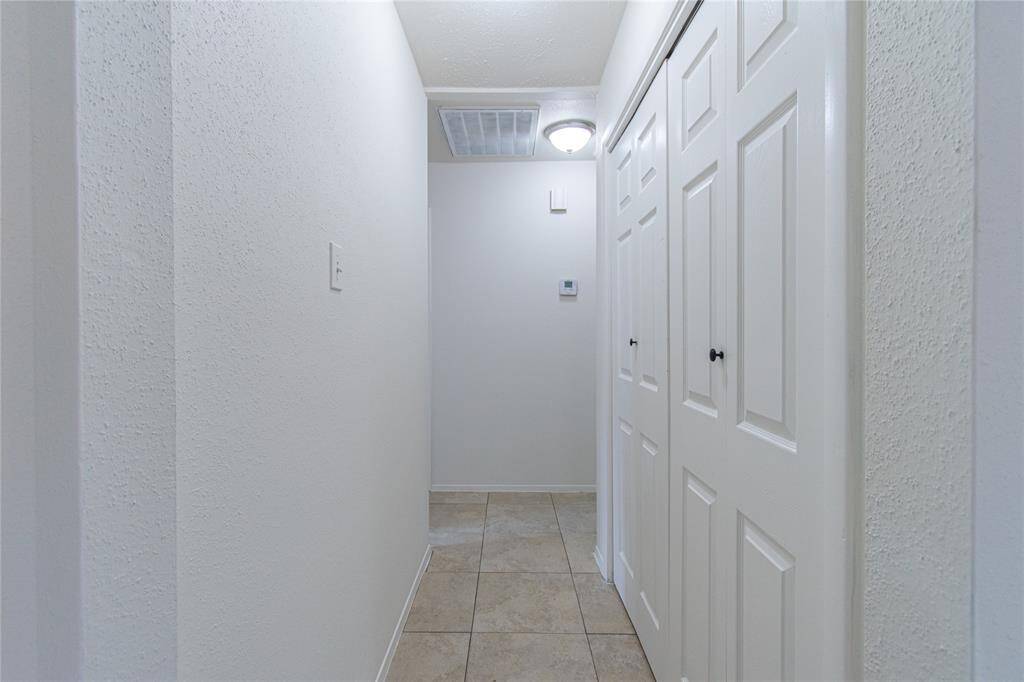 Bright, narrow hallway with light tile flooring and white walls. Features a ceiling light and closet doors on the right, creating a clean and functional entryway.