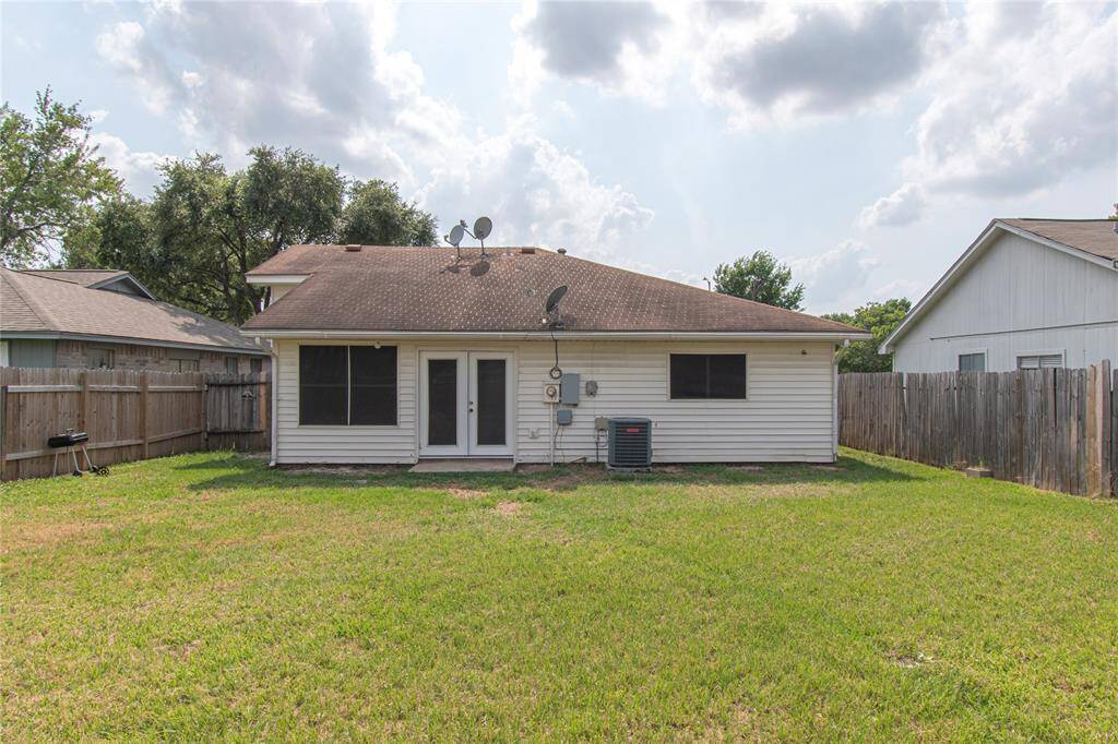 Spacious, fenced backyard with green grass, perfect for outdoor activities. The house has several satellite dishes and an HVAC unit visible, and there are neighboring houses on both sides.