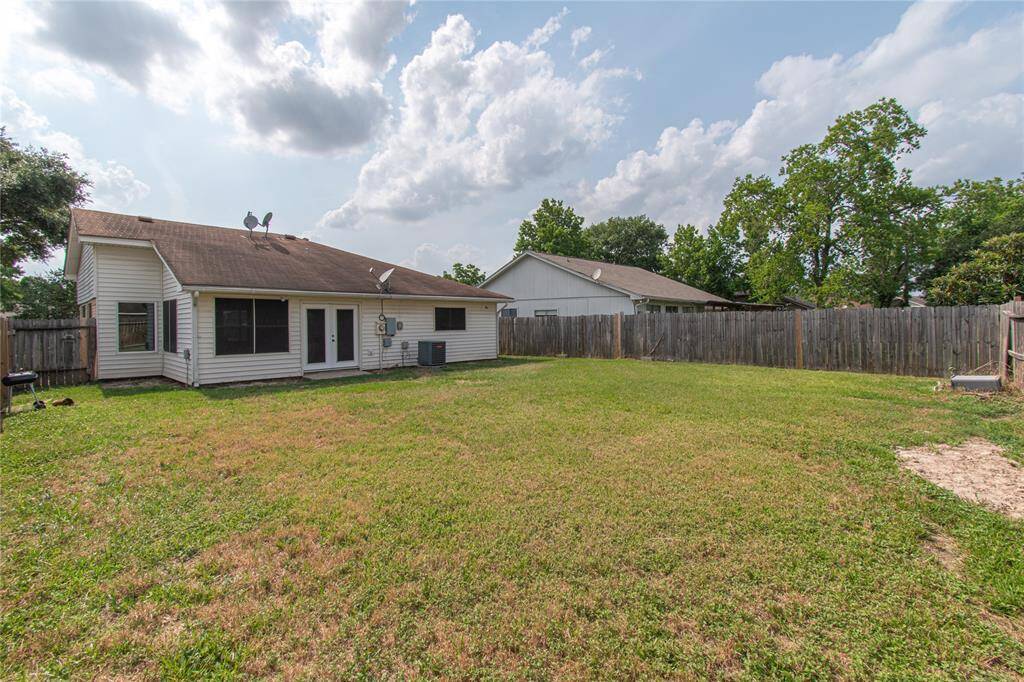 A spacious backyard with a well-maintained lawn, surrounded by a wooden fence. The back of the house features vinyl siding and multiple windows, providing natural light. Ideal for outdoor activities and privacy.