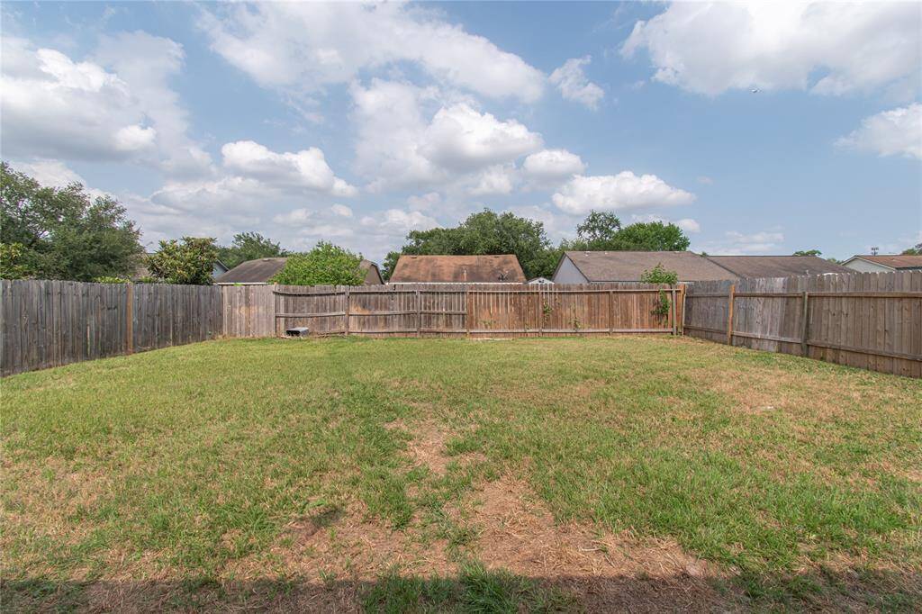 Spacious fenced backyard with a mix of green and dry grass, surrounded by wooden fencing, perfect for outdoor activities and privacy.