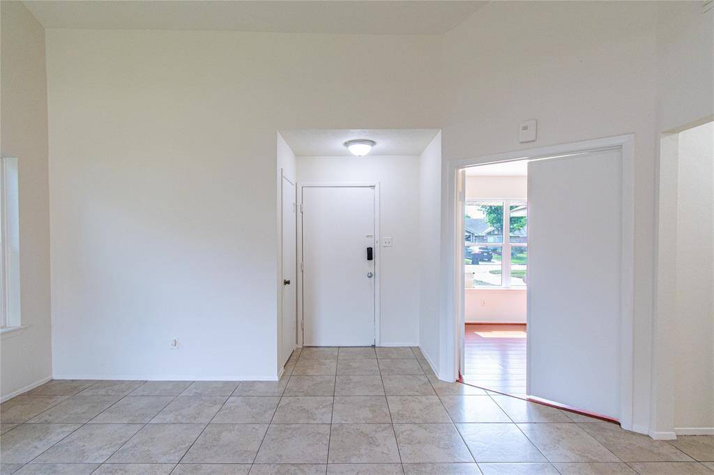 Bright entryway with tile flooring, neutral walls, and a door leading to a room with large windows.