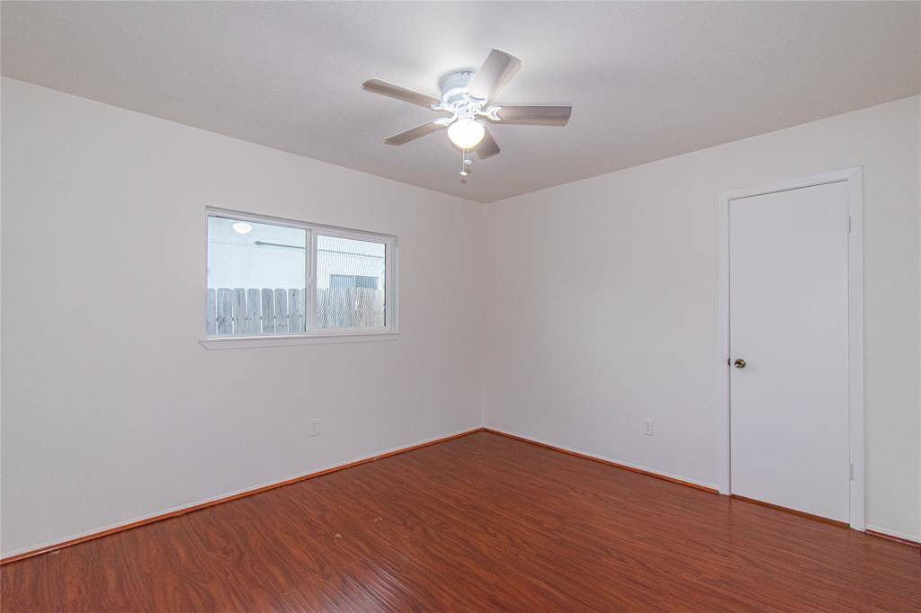 This room features hardwood floors, a ceiling fan with lighting, and a window providing natural light. The neutral walls offer a clean, versatile space, and there's a standard door for entry.