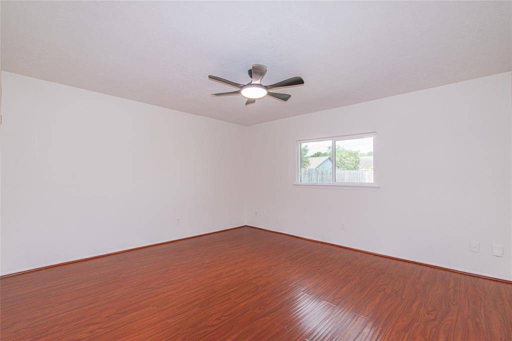 This room features sleek hardwood flooring, a modern ceiling fan, and a window providing natural light, creating a bright and airy space.