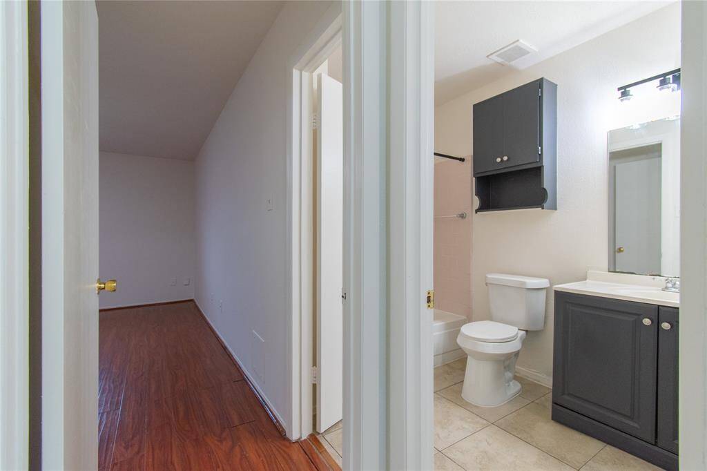 The bathroom features a tiled floor, a toilet, a dark cabinet, and a sink with a mirror.