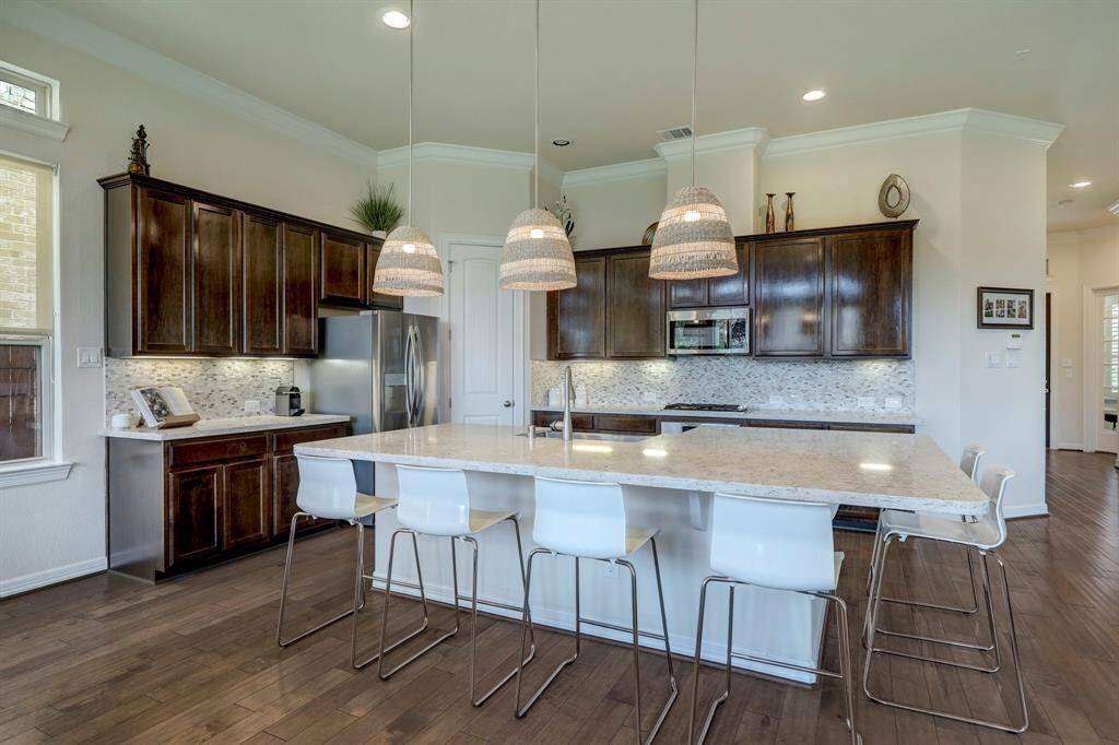 The Chef's Kitchen features high-ceilings, a spacious quartz countertop and a magnificent breakfast bar, exquisite cabinetry with ample storage, and elegant pendant lighting that enhances the overall aesthetic of the space.