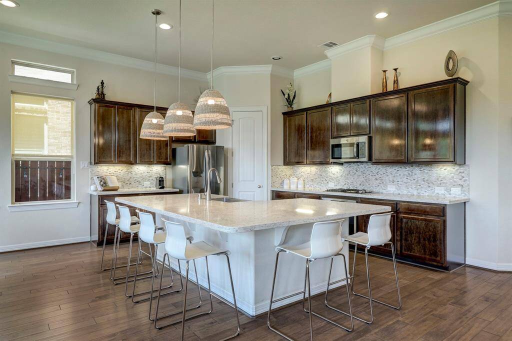 The kitchen showcases plentiful quartz countertops, an expansive breakfast bar area ideal for entertaining, generous storage capacity, stainless steel appliances, double ovens, and a sizable walk-in pantry.