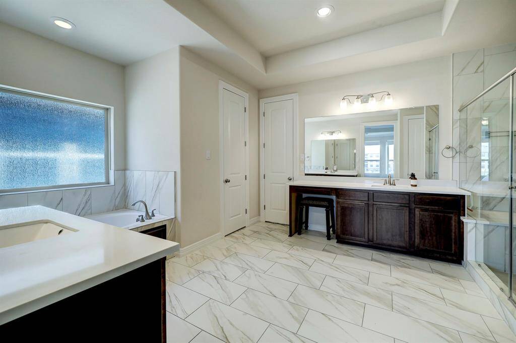 The spacious primary bath retreat showcases his and her vanities with large mirrors and ample lighting. It features high-recessed ceilings, a bathtub, frosted windows, and access to a huge spacious closet and direct access utility room.