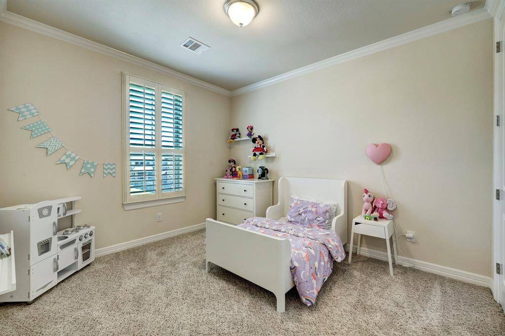 The first secondary bedroom presents a soothing neutral color palette that is also complemented by high ceilings with crown moldings, cozy carpeted floors and walk-in closet.