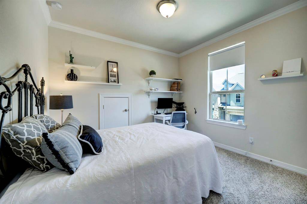 The Second secondary bedroom showcases notable features such as high ceilings adorned with double crown moldings, cozy carpeted floors, and a window that provides a pleasant view of the front yard and driveway.