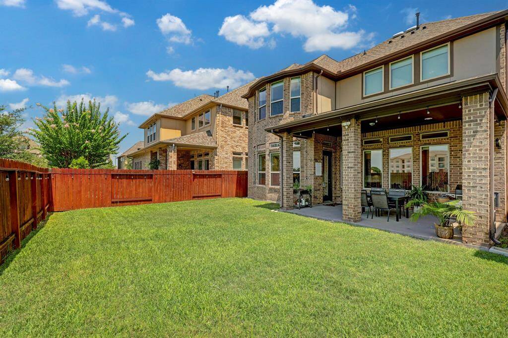 The lush green backyard is beautifully enclosed by a tall wooden fence with a rich wood stain, ensuring both privacy and convenience.