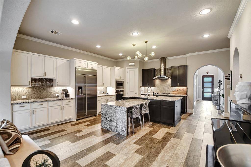 This modern kitchen features sleek white cabinetry, a large island with seating, and elegant lighting. The open layout flows into the living area with ample natural light, perfect for entertaining.