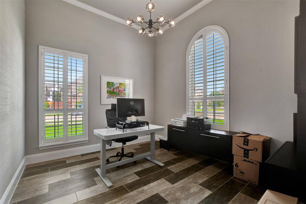 A bright home office with large windows and shutters, providing ample natural light. The room features beautiful and modern floors and ample space.