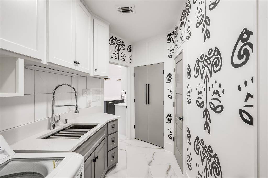 Designer wall covering adds panache to the laundry/mud room. This utilitarian space includes a double door food pantry, full-sized sink with industrial pull-down faucet, new wash machine and dryer, cleaning supply closet, and half bathroom.