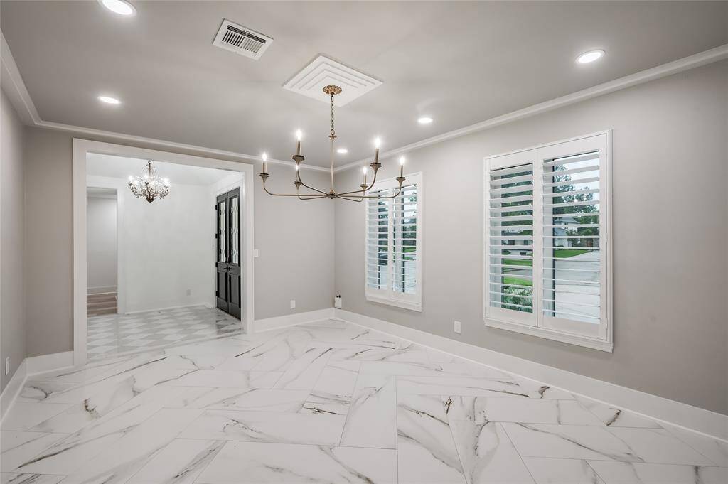 Spacious dining room features contemporary chandelier, recessed lighting, and large windows with plantation shutters.