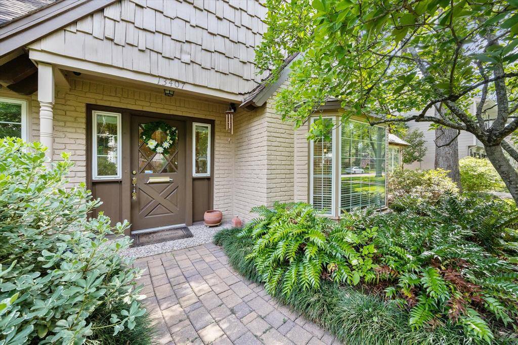 The front door is beautifully framed by a covered porch, creating a welcoming entryway that’s both elegant and inviting. Surrounded by lush landscaping, this charming façade offers a perfect blend of curb appeal and natural beauty.