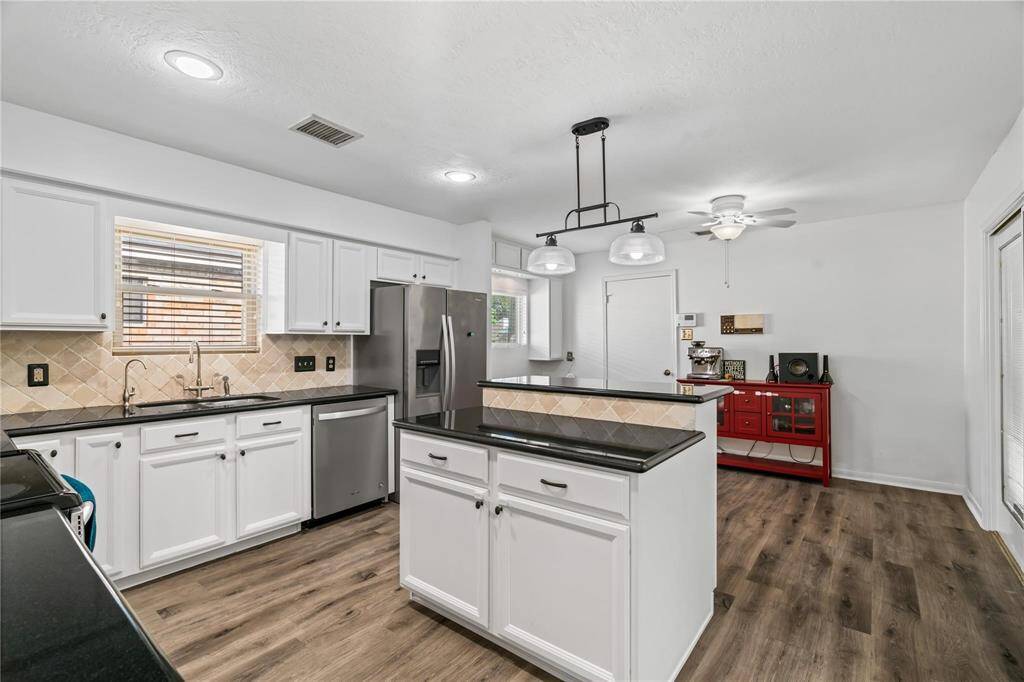 This kitchen features modern stainless steel appliances, white cabinetry, and black countertops. It has a central island with pendant lighting and wood-style flooring, creating a stylish and functional space.