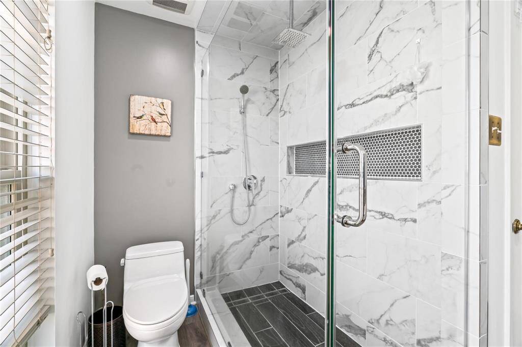Modern bathroom featuring a sleek glass shower with marble tiles and a rainfall showerhead, complemented by a minimalist toilet and stylish decor.