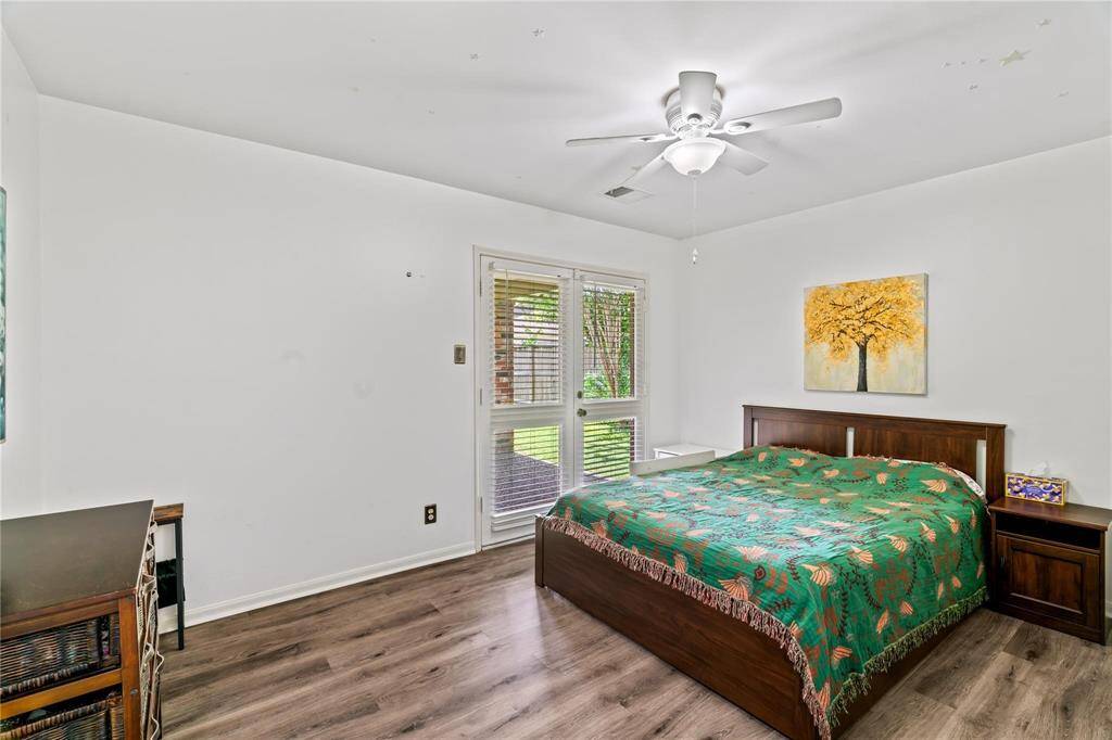 This is a bright bedroom with a large window, featuring a ceiling fan, hardwood flooring, and a simple, modern decor.