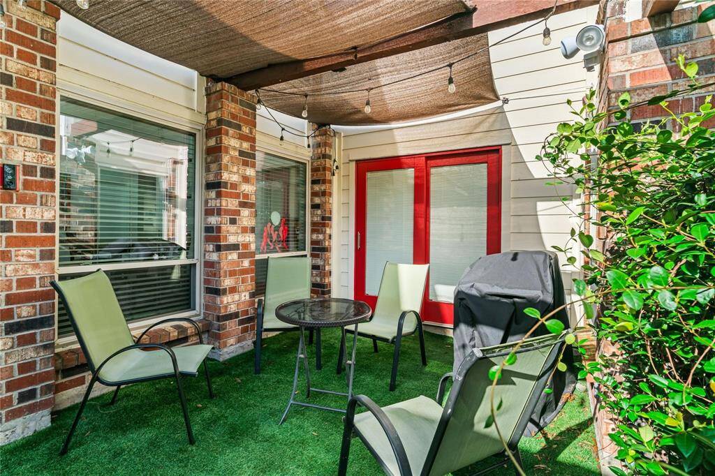 Charming patio with red French doors, shaded pergola, and green artificial turf. Features comfortable seating and a grill, ideal for outdoor relaxation and entertaining.