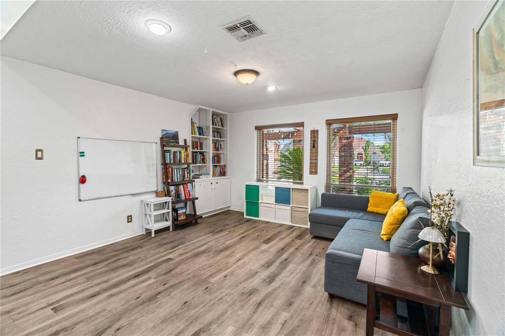 Bright, inviting living space with large windows, wood flooring, and a cozy sectional. Features include a built-in bookshelf, storage, and a whiteboard, ideal for a home office or study area.
