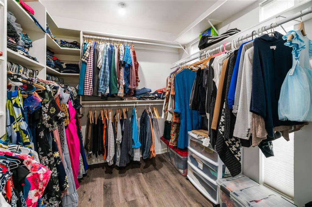 This spacious walk-in closet features ample hanging space, shelving, and drawers for organized storage. It has a bright interior and hardwood flooring, offering a tidy and functional design for clothing and accessories.