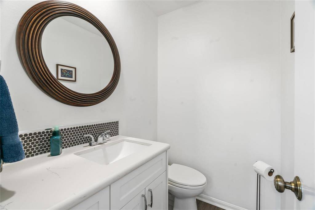 This bathroom features a modern design with a white vanity, a circular mirror, and a subtle tile backsplash. The room is bright and clean, with minimal decor for a sleek look.