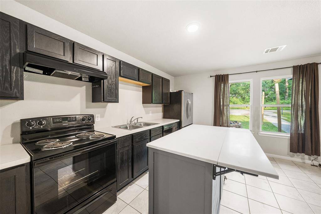 Electric stove and dark cabinetry. Windows provide ample natural lighting.