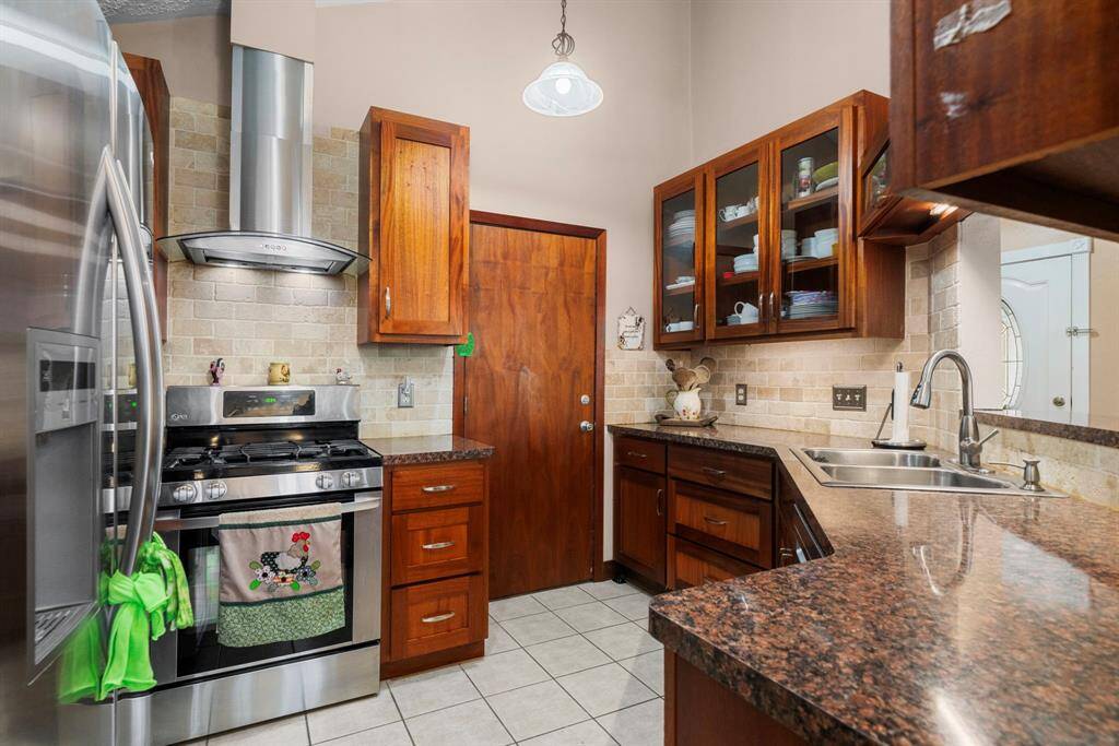Fabulous remodeled kitchen with custom cabinets, stainless steel appliances, a stylish vent hood, elegant countertops, a chic backsplash, and more.