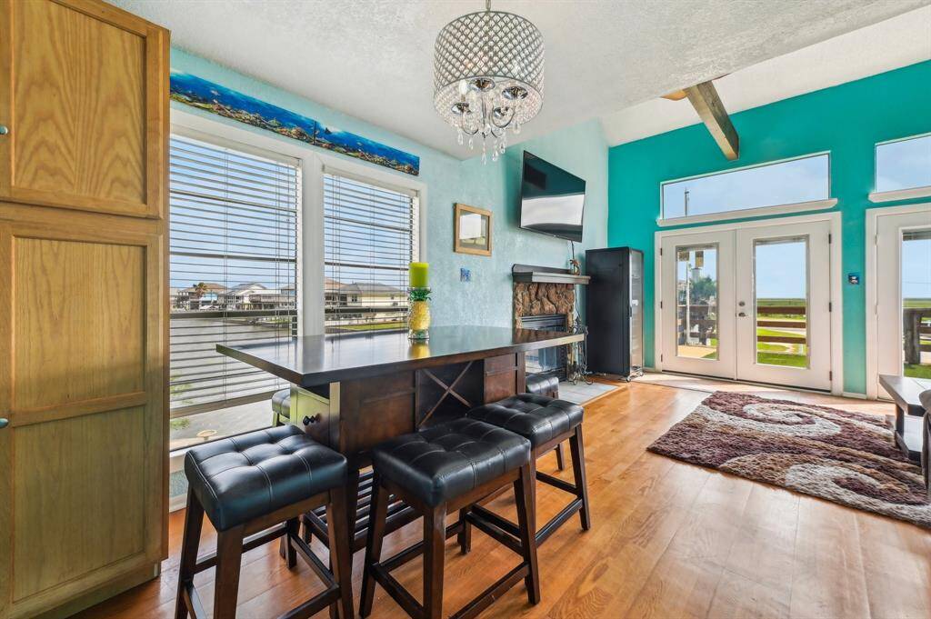 This bright and airy living space features high ceilings, a cozy seating area with plush couches, and a stylish open kitchen with modern appliances. The room is accented by vibrant turquoise walls and decorative wall art, creating a welcoming and lively atmosphere. Large windows allow plenty of natural light to fill the space.