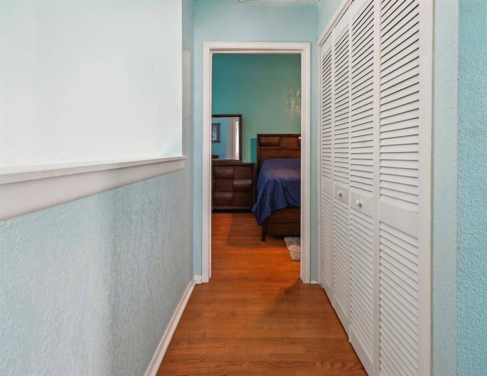Cozy bedroom with wooden flooring, featuring a large bed with a blue-striped comforter. The room includes a walk-in closet and an attached bathroom, decorated with rustic accents. Wall art and decor add character to the space.