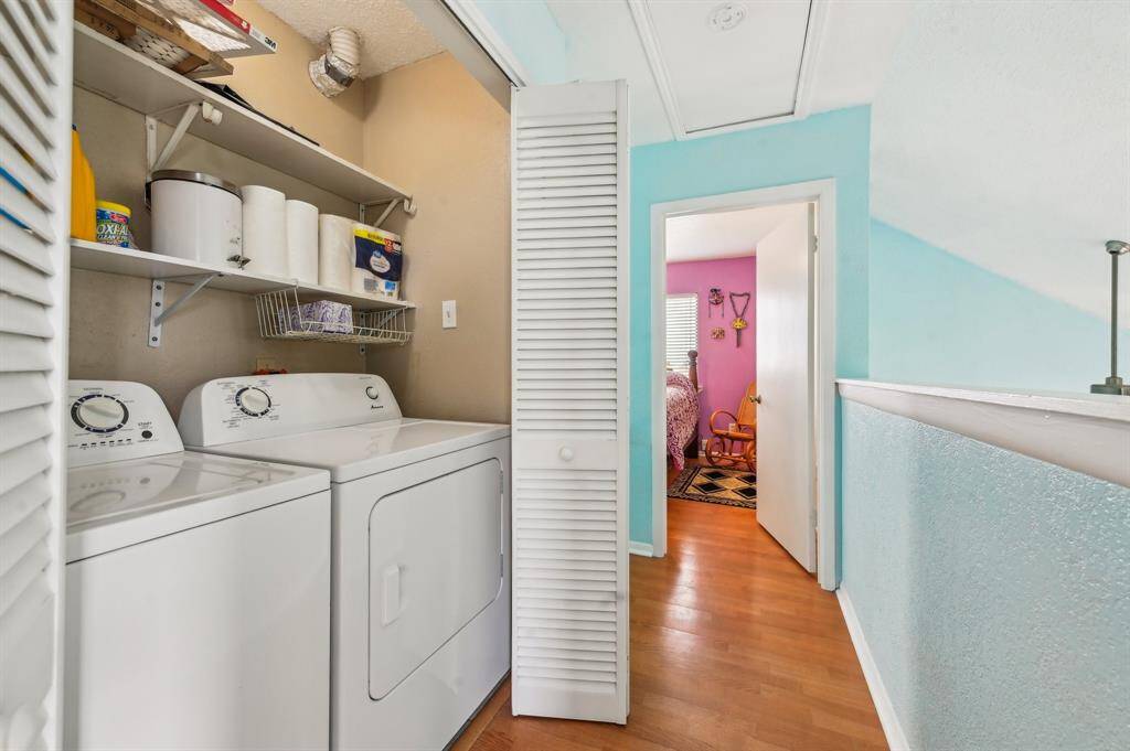 This bedroom features a vibrant teal accent wall, ceiling fan, and wood flooring. It includes a spacious bed and matching dresser with a mirror. A small closet with white louvered doors adds storage. Bright and inviting space.