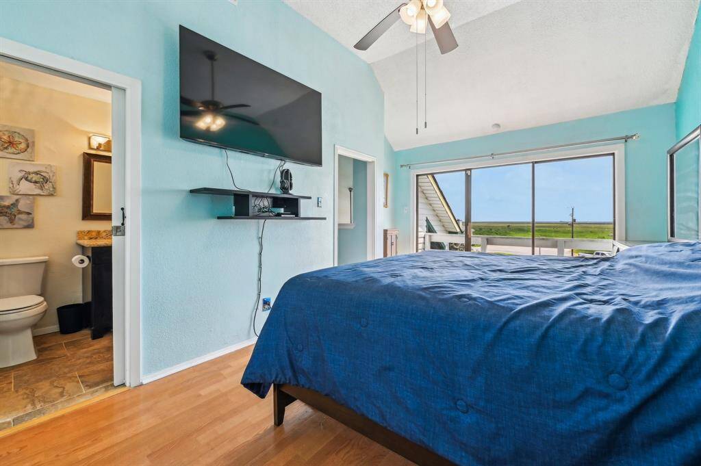 This photo shows a compact laundry area with a washer and dryer tucked into a hallway with wooden floors. Shelving above provides storage for household items. A colorful bedroom is visible through an open door, adding a vibrant touch to the space.