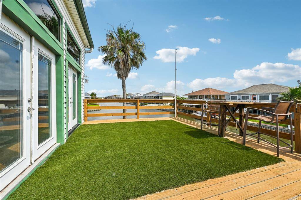 This photo shows a covered outdoor patio with white siding, featuring a dining table and chairs, ceiling fans, and a view of a grassy area and water. Perfect for entertaining and enjoying the outdoors.