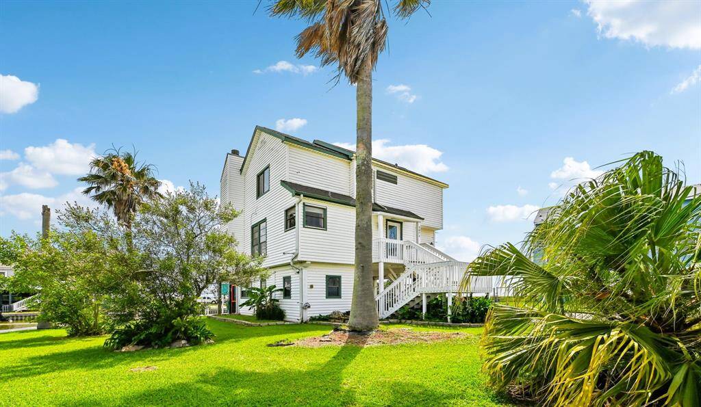 This home features a charming elevated design with a spacious driveway and lush green lawn. It offers scenic waterfront views, enhanced by a picturesque sunset backdrop. Ideal for those seeking a serene, coastal lifestyle.
