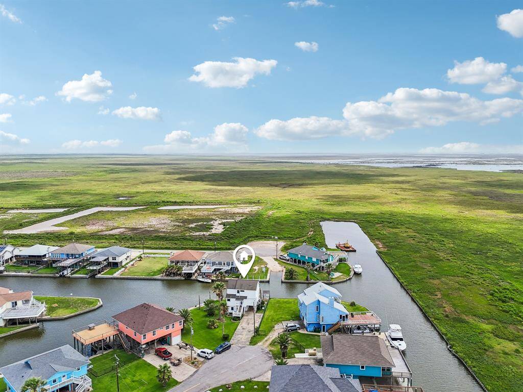 This photo showcases a serene neighborhood with waterfront homes, featuring colorful houses along a canal. The area is surrounded by lush green fields and offers expansive views of open land under a vibrant sky. Ideal for those seeking a tranquil, scenic setting.