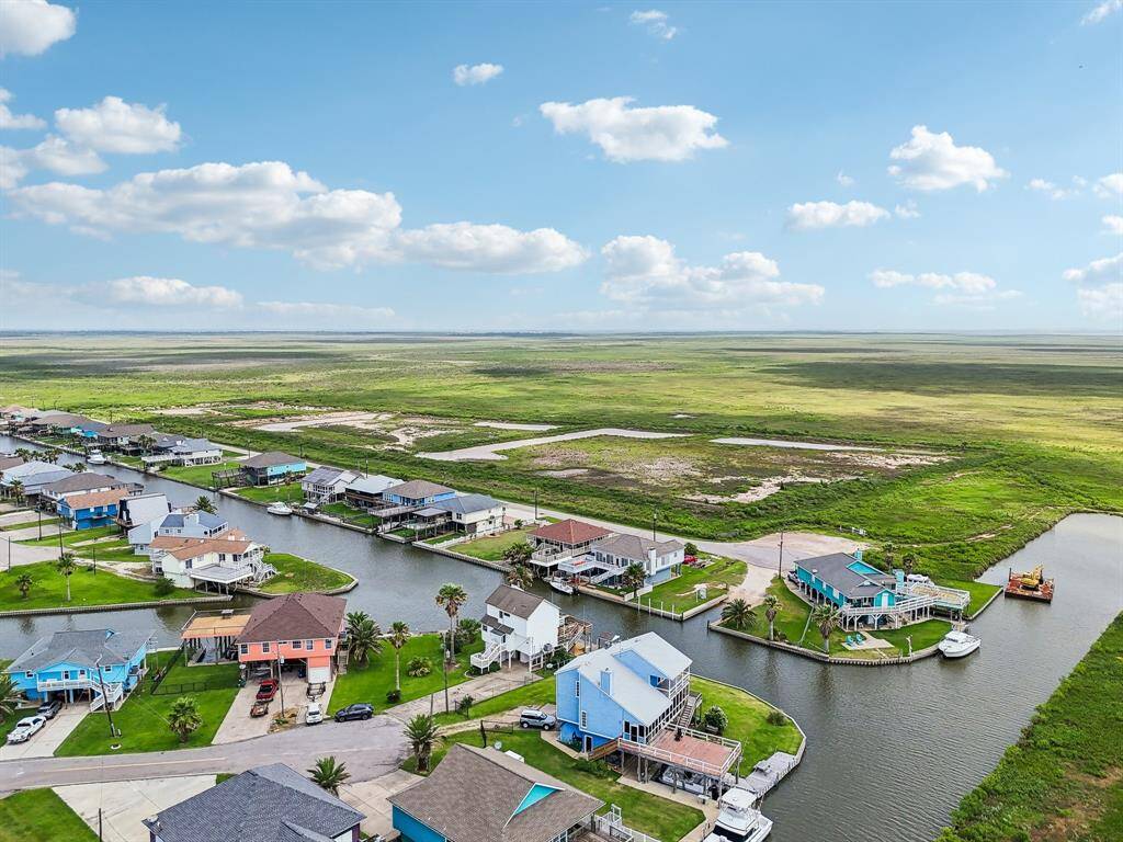 This aerial photo showcases a scenic waterfront neighborhood with colorful homes along a canal, offering expansive views of lush green marshlands and open skies. Ideal for those seeking a serene, picturesque setting.