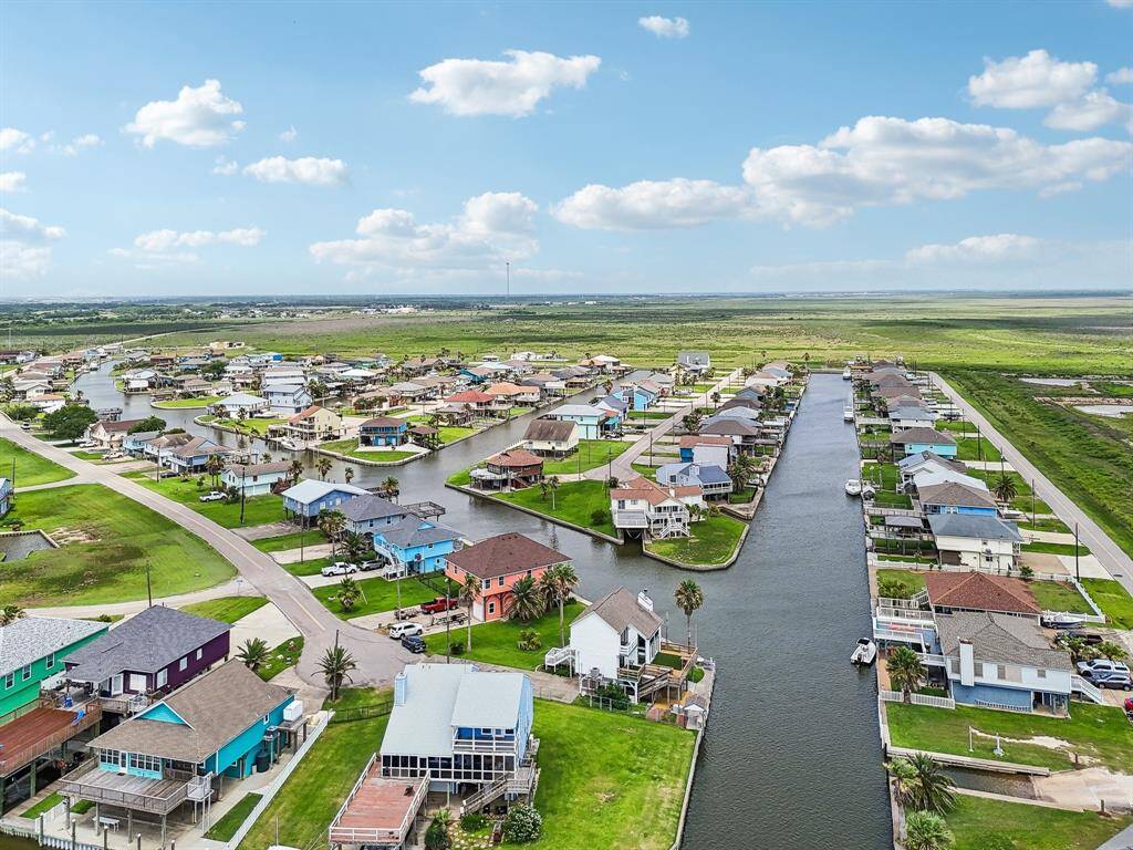 This photo shows a serene waterfront community with colorful houses along a canal. Each home has direct water access, surrounded by lush greenery and expansive open land, under a bright blue sky. Ideal for those seeking a peaceful, scenic environment with nautical charm.