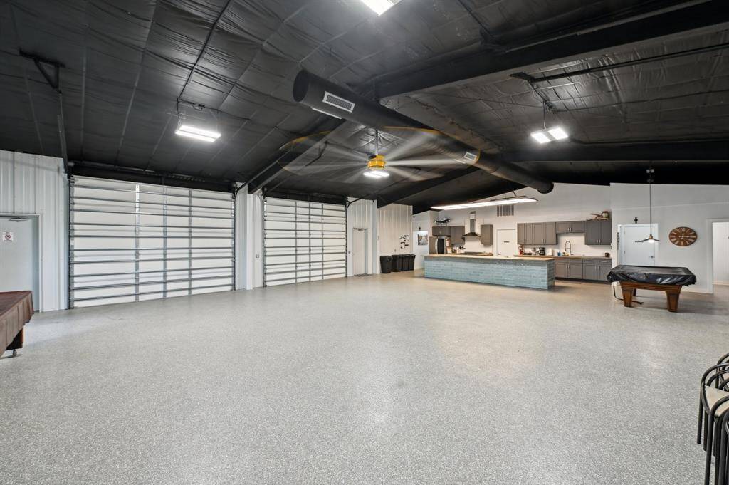 This property features a spacious, modern metal building with large garage doors, set amidst expansive grassy fields. The structure is well-maintained, with a paved walkway leading to the entrance, and a fenced area suggesting security and privacy.