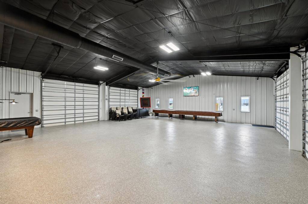 This spacious shop features a sleek, modern design with high ceilings, ample lighting, and  concrete floors. It includes multiple large garage doors and a stylish kitchenette with contemporary cabinetry, offering plenty of room for vehicles and leisure activities.