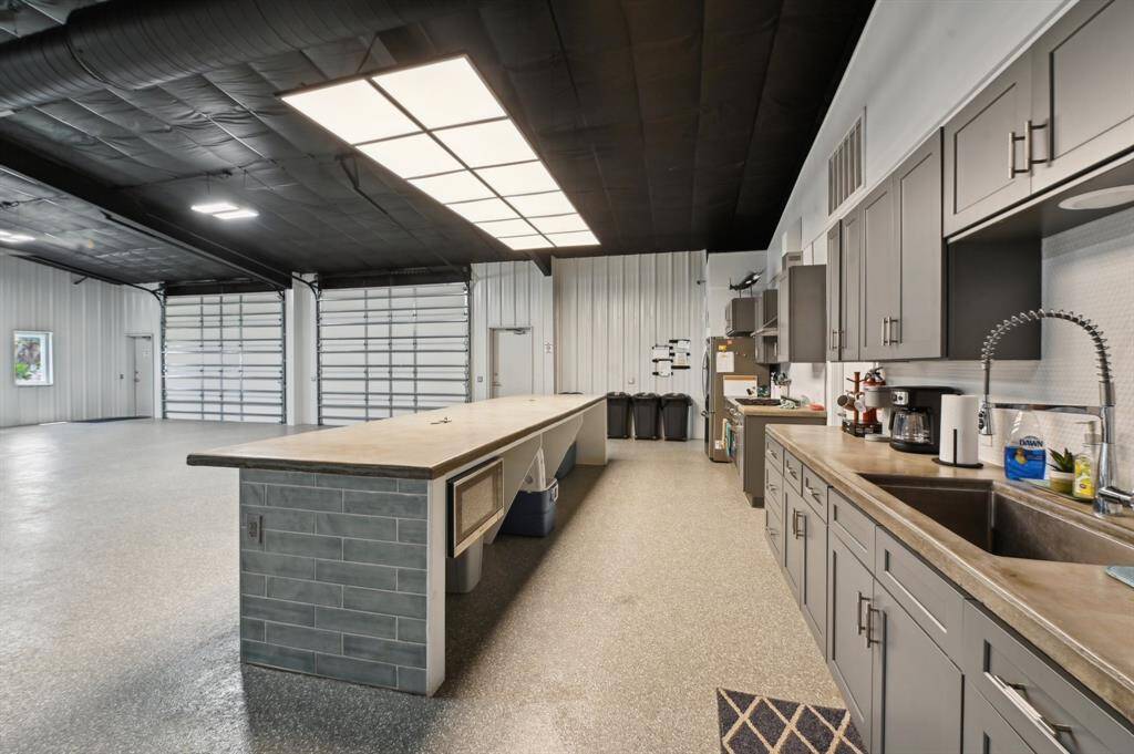 Modern industrial kitchen with stainless steel appliances, gray cabinetry, and ample counter space. High ceilings feature exposed ductwork, and large windows provide natural light. Ideal for cooking enthusiasts.
