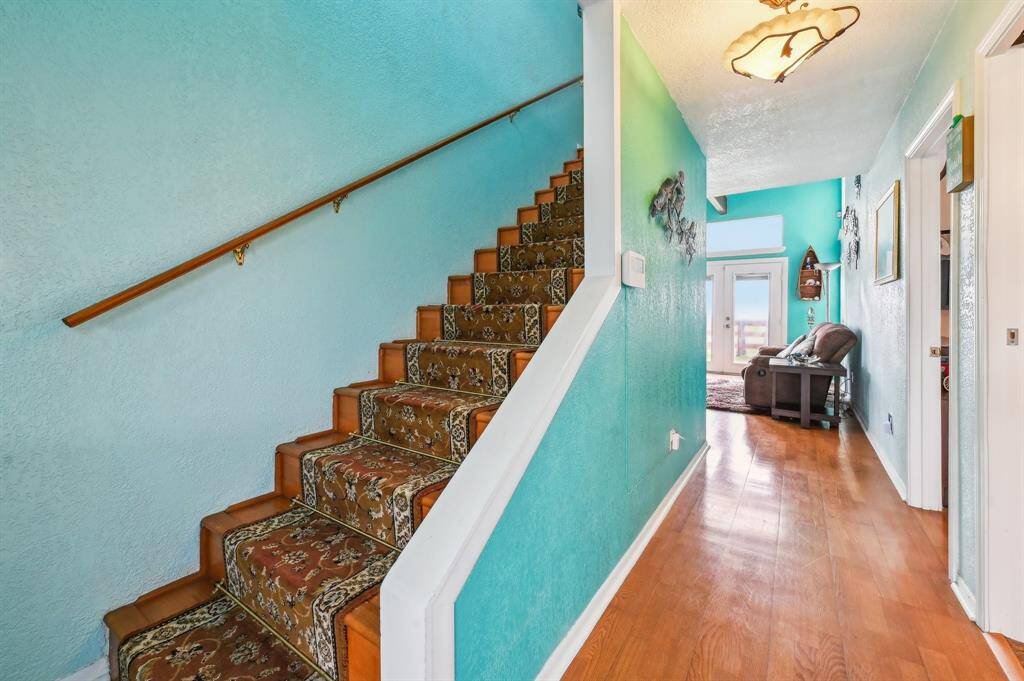 Charming multi-story home with white siding and green trim, featuring a spacious yard adorned with palm trees. The property includes a large staircase leading to an elevated entrance, set against a bright blue sky backdrop. Ideal for those seeking a tropical feel.