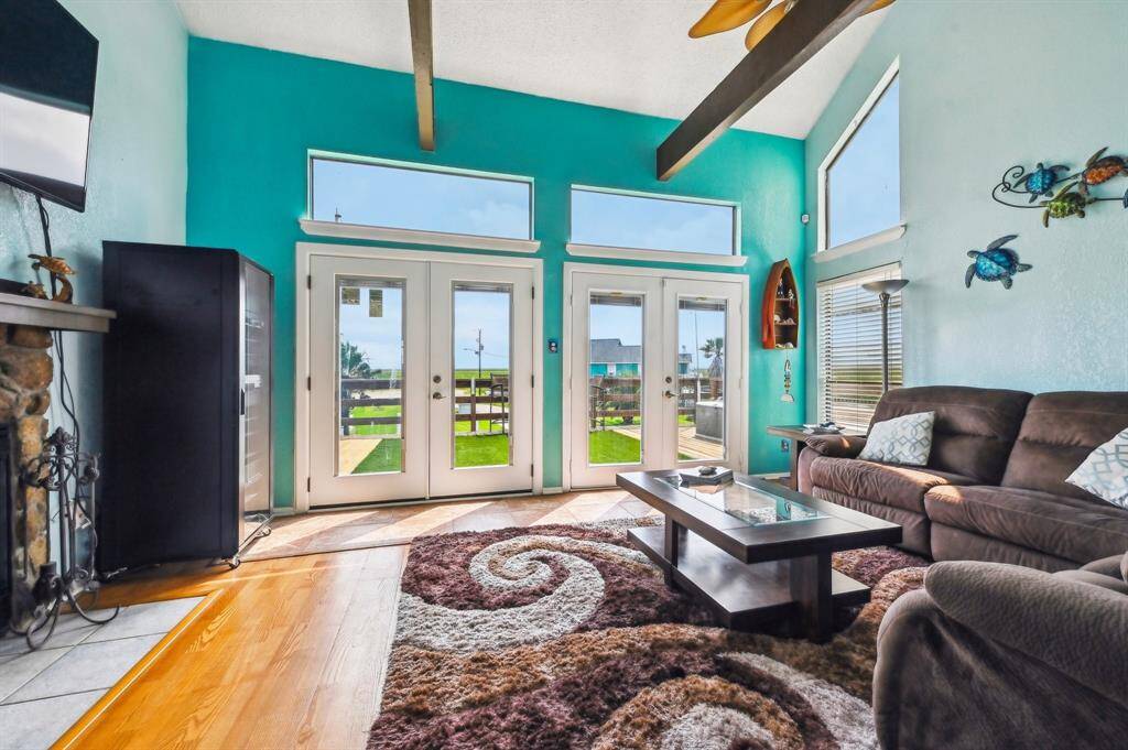 This photo showcases a vibrant hallway with turquoise walls and warm wooden flooring. A staircase with a colorful carpet leads upstairs, and the hallway opens into a bright living area with large windows, offering a welcoming and spacious feel.