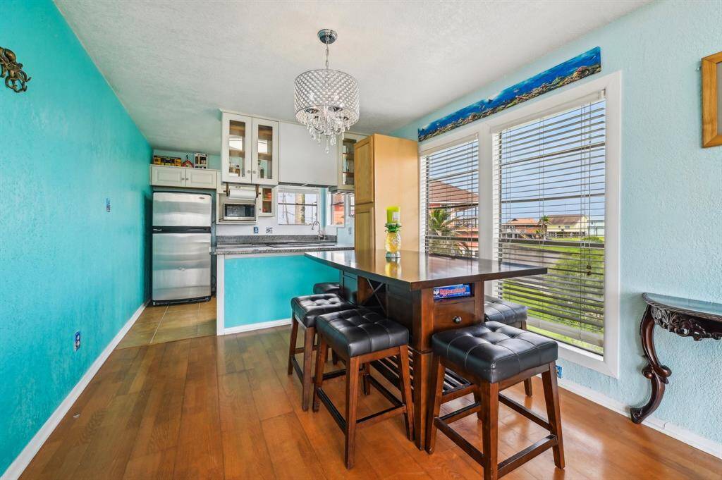This bright living room features high ceilings with exposed beams, large windows, French doors leading to a patio, and vibrant turquoise walls. It's furnished with a cozy brown sofa, a stylish coffee table, and has a unique, decorative rug.