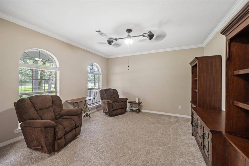The formal living room is a wonderful space to gather and visit with guests, featuring plush carpet, neutral paint, a modern lit ceiling fan, and arched windows with lovely views of the front yard.