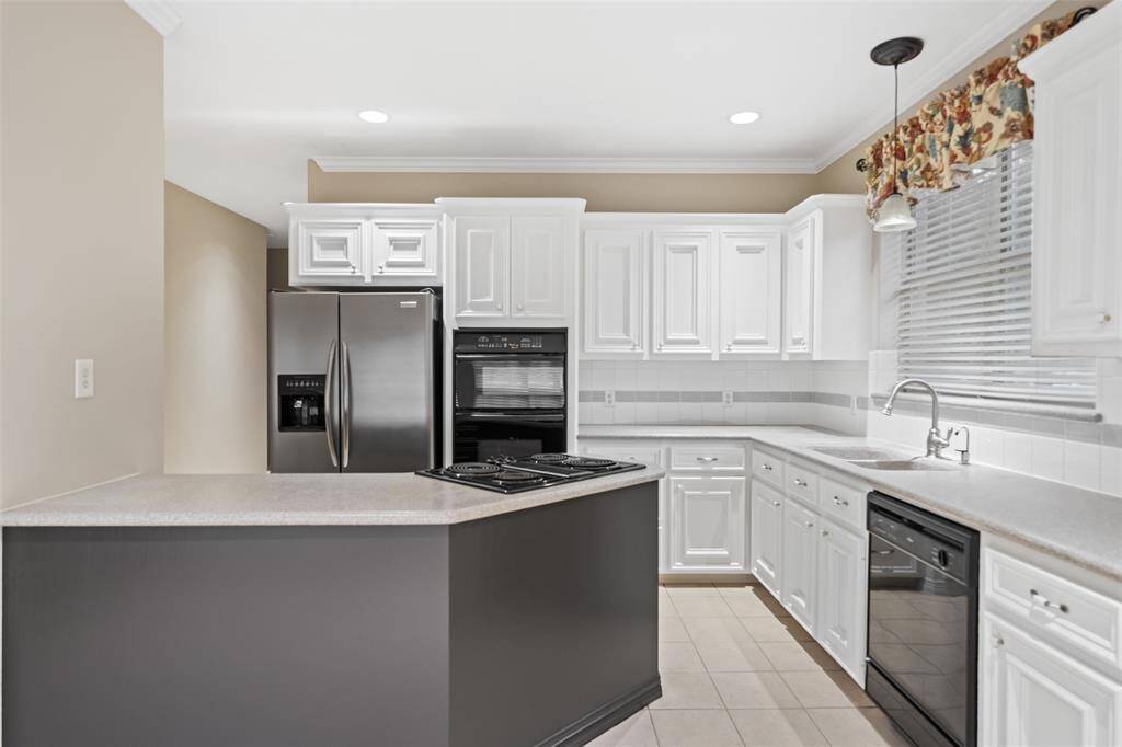 Ditch the takeout and enjoy cooking at home in this fully equipped kitchen featuring crisp white cabinetry, Corian countertops, classic tile backsplash, sleek black appliances, a spacious pantry, and a nearby wet bar or butler’s pantry for added convenience.