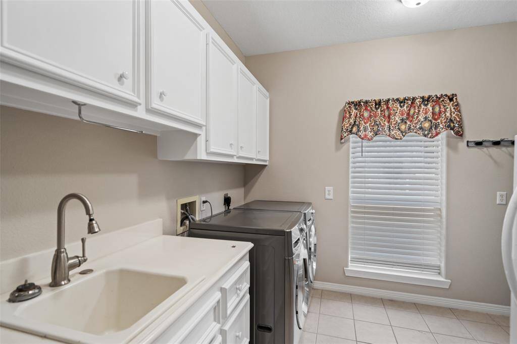 The oversized utility room offers built-in cabinetry for household storage, a convenient sink, both gas and electric dryer connections, and ample space for an extra freezer or refrigerator.