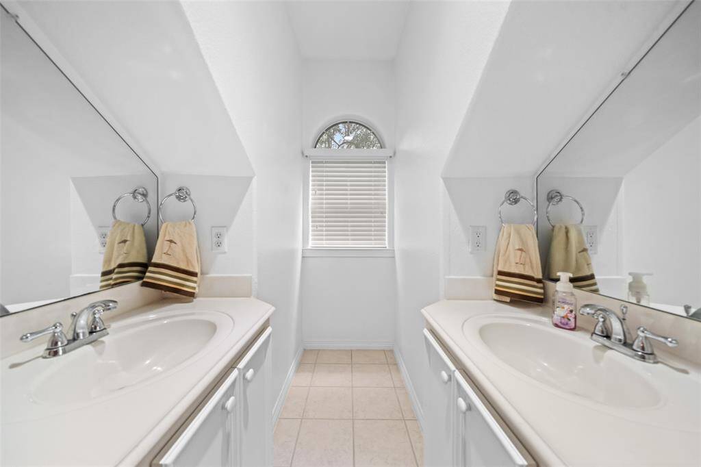 The guest's Hollywood style bathroom features a unique split vanity design with dual sinks, plenty of storage, and a charming arched window that brings in soft natural light. It's perfect for sharing without compromising space.