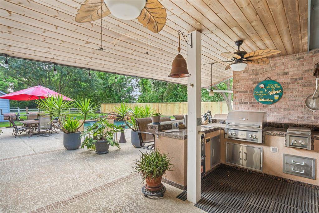 Fire up the grill and enjoy outdoor entertaining at its finest in this fully equipped summer kitchen, complete with built-in stainless appliances, including a two-burner cooktop, grill, and sink with hot and cold water—plus granite countertops and bar seating. All of it sits under a wood-slat covered patio with surround sound and cooling fans, keeping the good times going rain or shine.