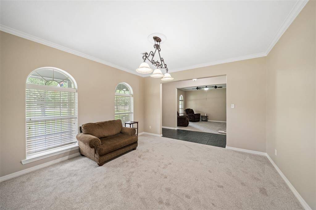 The formal living and dining rooms provide elegant spaces to gather, featuring arched windows for natural light, soft neutral finishes, plush carpet, crown molding, and updated overhead lighting in both rooms.